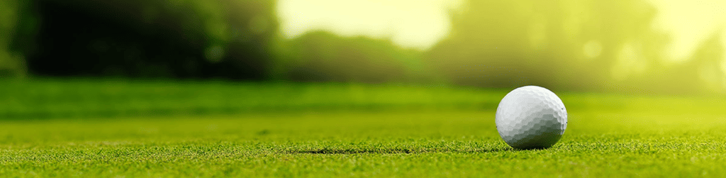 a close up shot of a golf ball on a green field with some blurred trees in the background