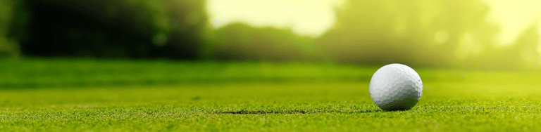 a close up shot of a golf ball on a green field with some blurred trees in the background